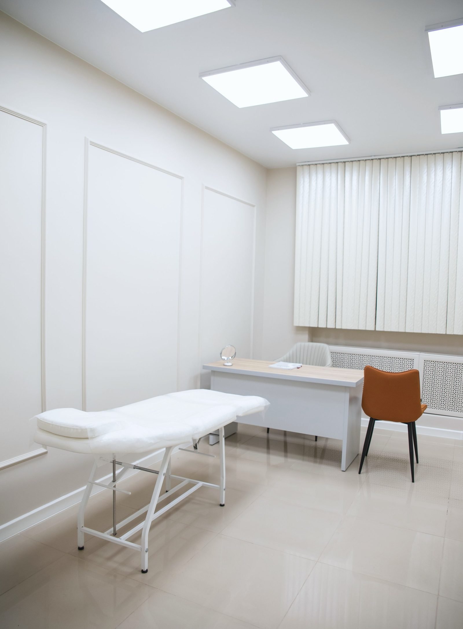 An empty exam room with a padded table, a desk and a chair