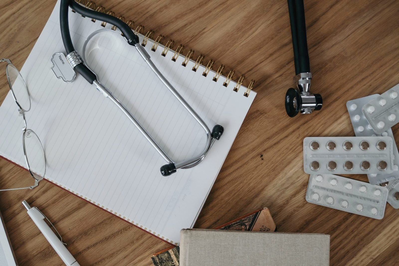 A stethoscope, a notepad and reading glasses on a wooden desk
