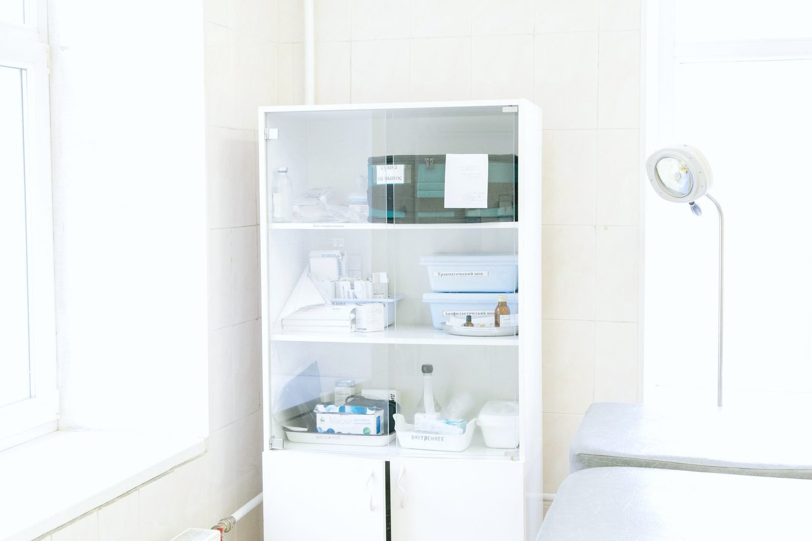 A glass fronted clinic cabinet holding trays and supplies
